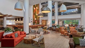 Eine geräumige Lobby mit mehreren Sitzbereichen, einer Bar und einer Treppe zu den oberen Stockwerken.