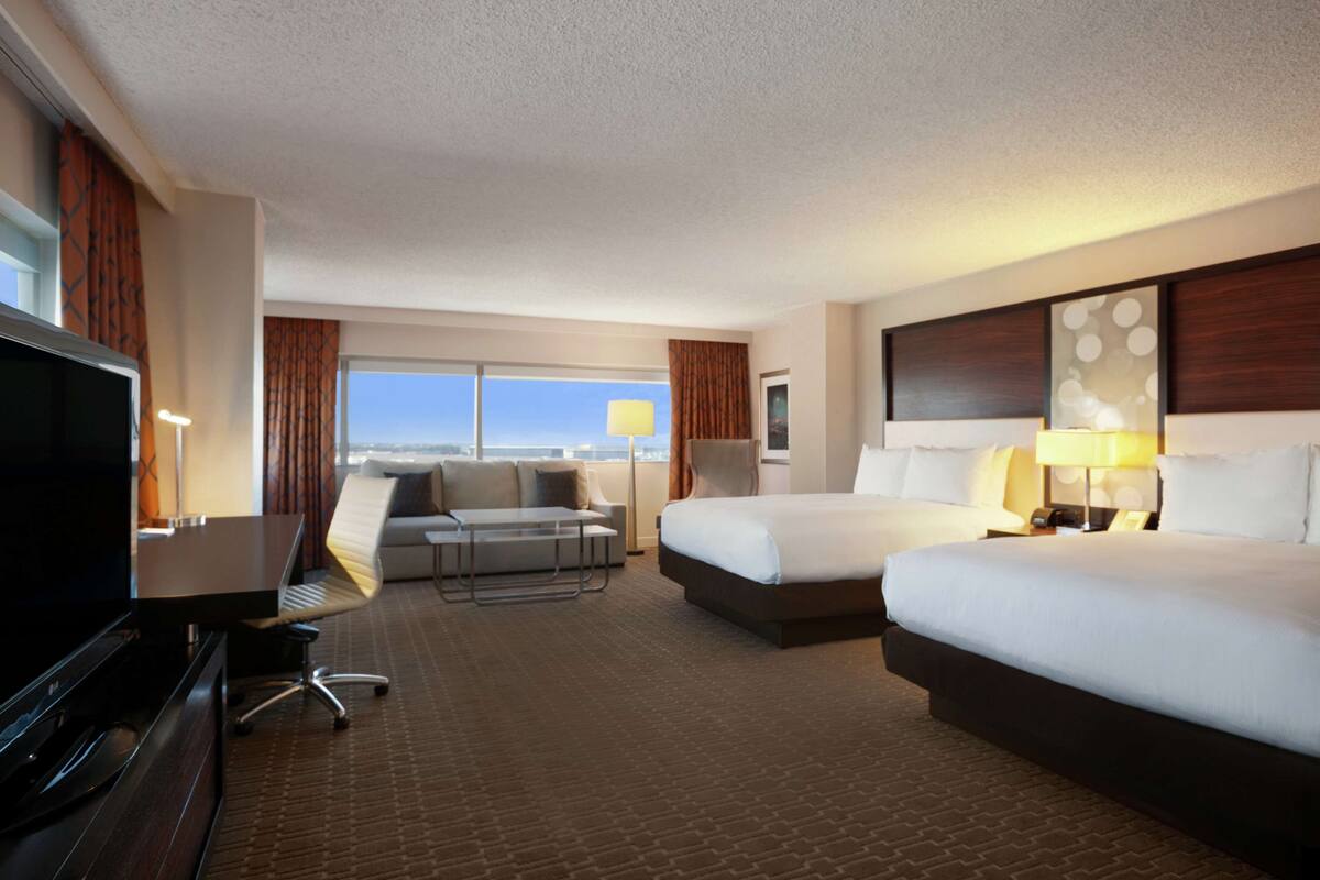 Una habitación de hotel con una cama grande, una cama más pequeña, un escritorio con ordenador, televisión, sofá y ventana con vistas.