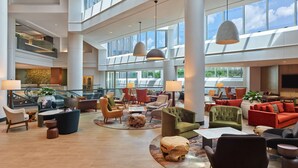 Eine geräumige Lobby mit mehreren Sitzbereichen, großen Fenstern und modernen Leuchten.