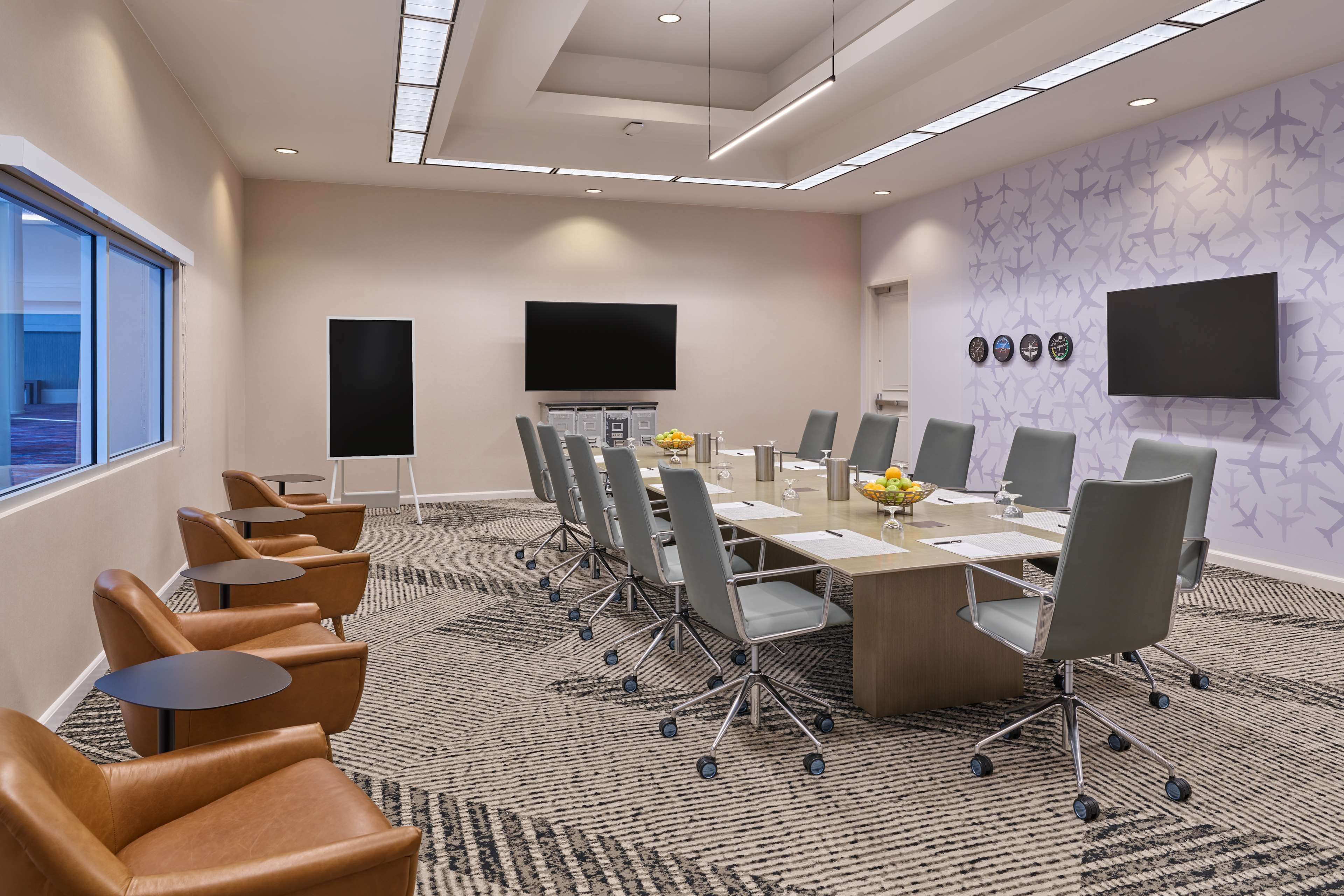 A conference room with a long table, multiple chairs, a flat-screen TV, and a patterned carpet.