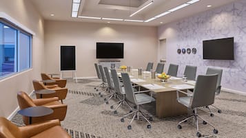 A conference room with a long table, multiple chairs, a flat-screen TV, and a patterned carpet.