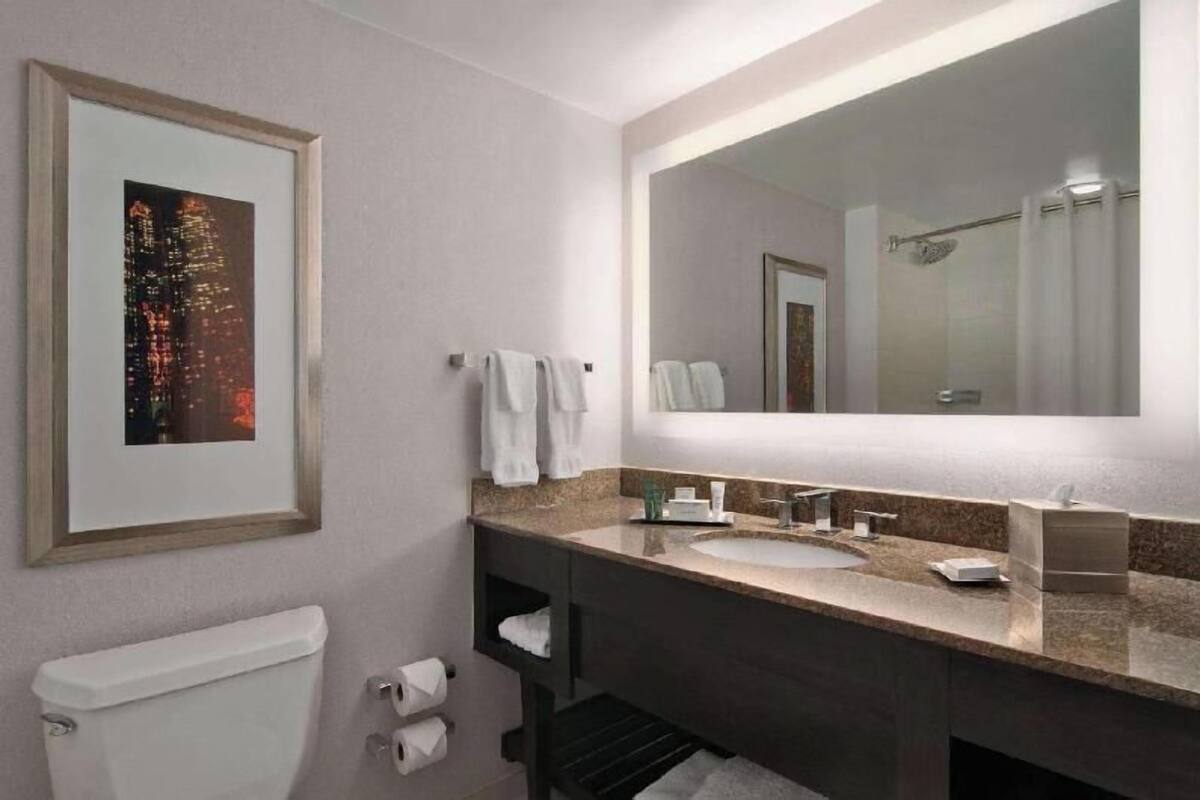 Un baño moderno con un espejo grande, un lavabo y un inodoro.