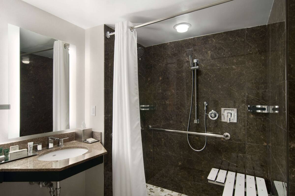 Un baño moderno con un lavamanos grande, una ducha con cabezal de ducha manual y una barra de apoyo.
