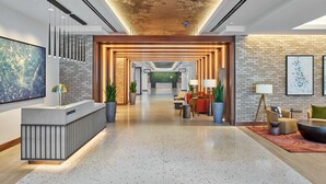 Eine moderne Hotelhalle mit Empfangstresen, Sitzgelegenheiten und einem großen Kunstwerk an der Wand.