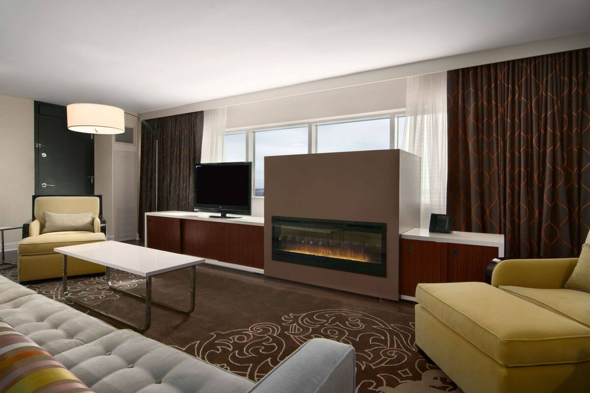 Una sala de estar moderna con sofá, sillón, televisor de pantalla plana, chimenea y un ventanal con cortinas.