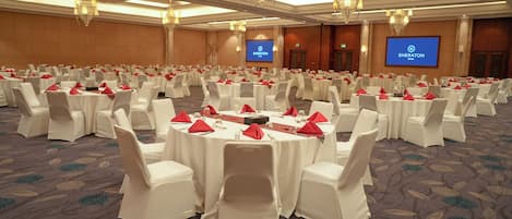 Une grande salle de conférence avec des tables rondes, des chaises blanches et des serviettes rouges.