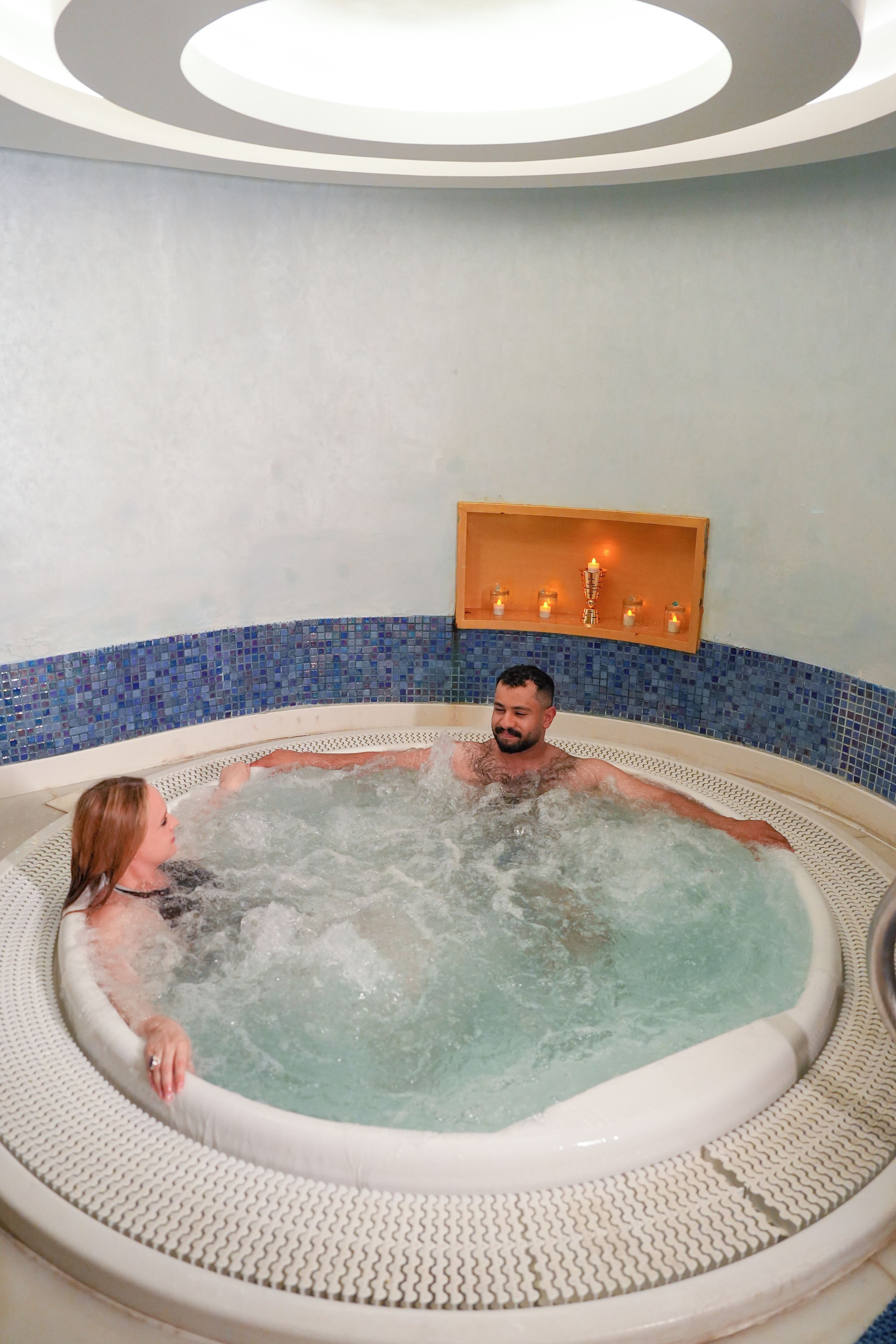 Un jacuzzi con interior de azulejos y un estante de madera con velas.