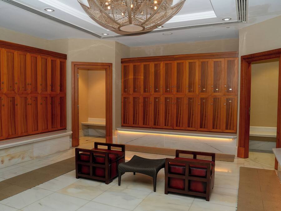Un pasillo espacioso con paneles de madera, una zona de estar con una mesita y sillas, y un techo con tragaluz e iluminación decorativa.