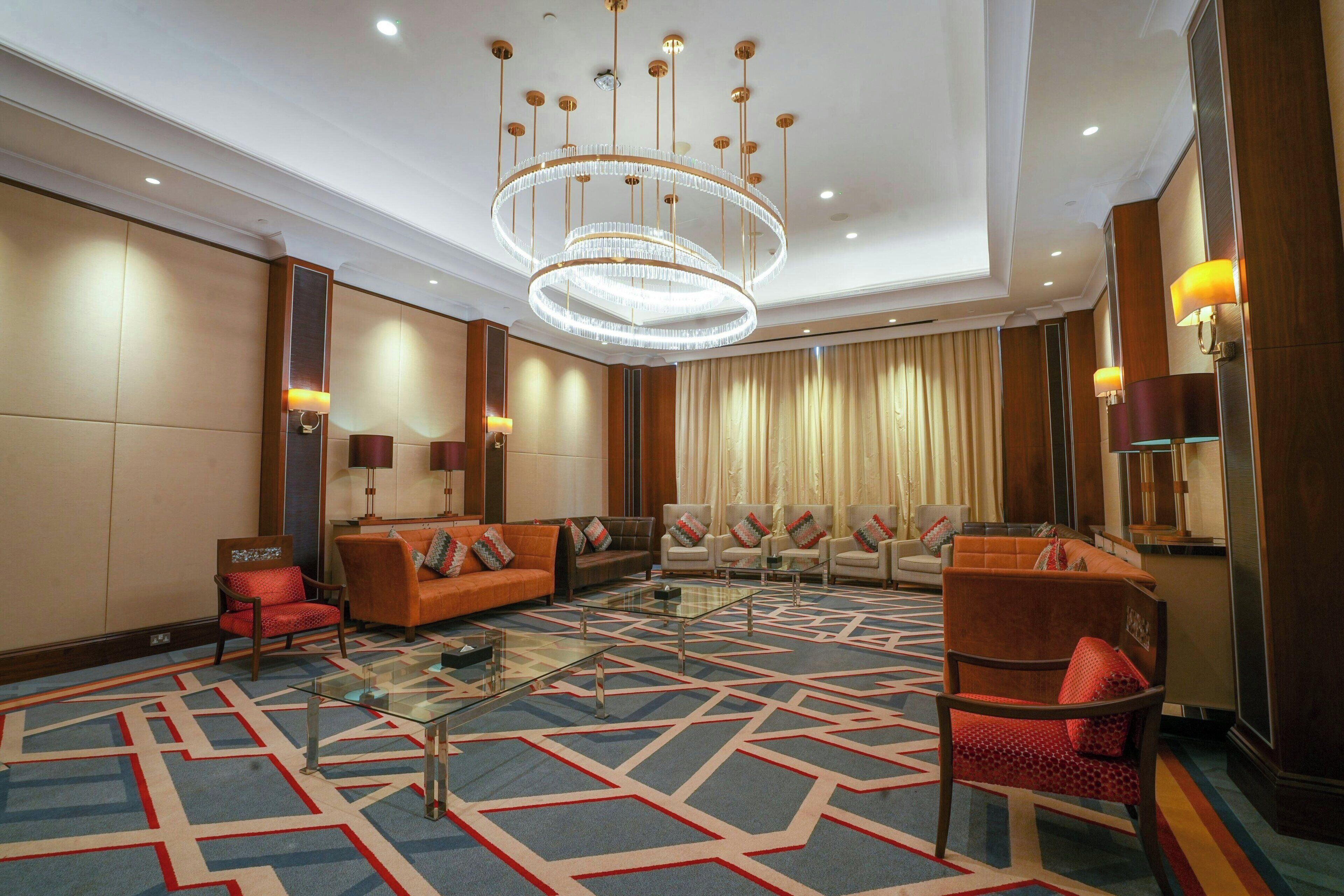 A hotel lobby with a modern chandelier, seating area with sofas and armchairs, and a patterned carpet.