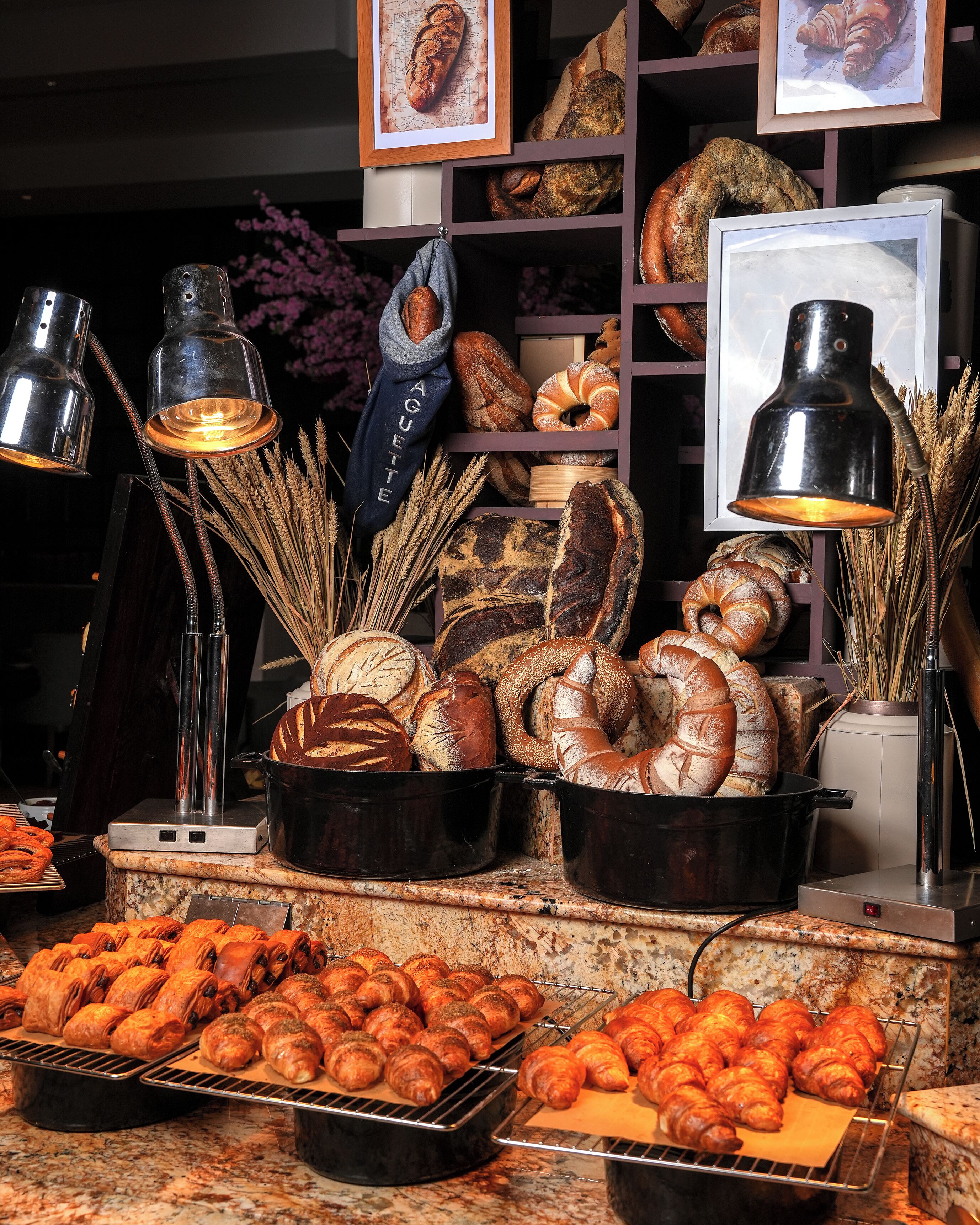 A bakery display with various breads and pastries, including croissants and baguettes, under black lamps.