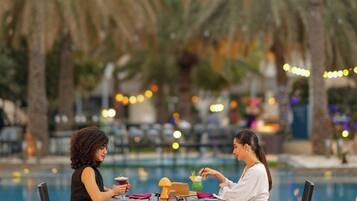 Two people seated at a table by a poolside with palm trees in the background.