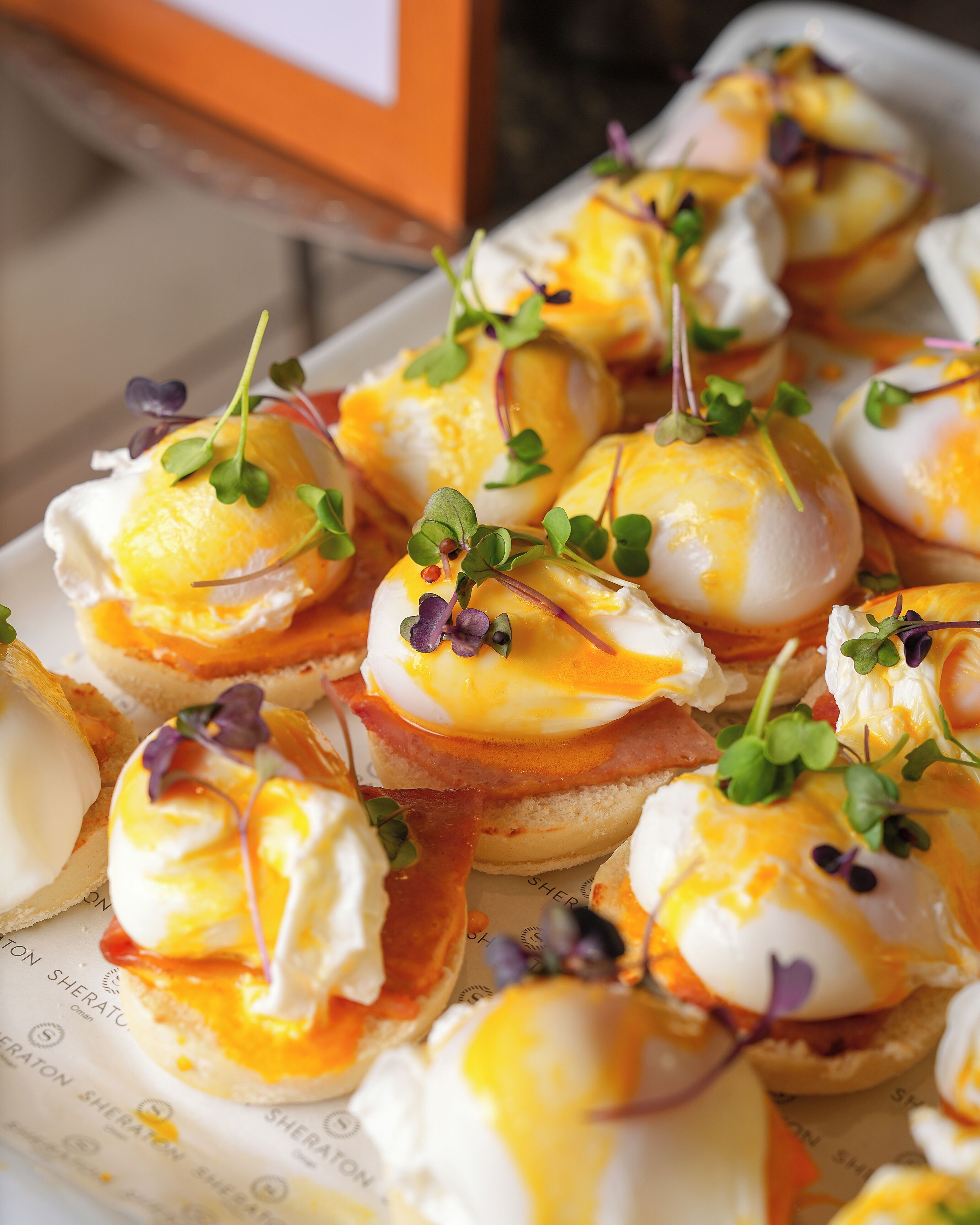 A tray of poached eggs with hollandaise sauce and microgreens on toast.