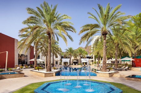 A pool area with palm trees, lounge chairs, and a fountain.