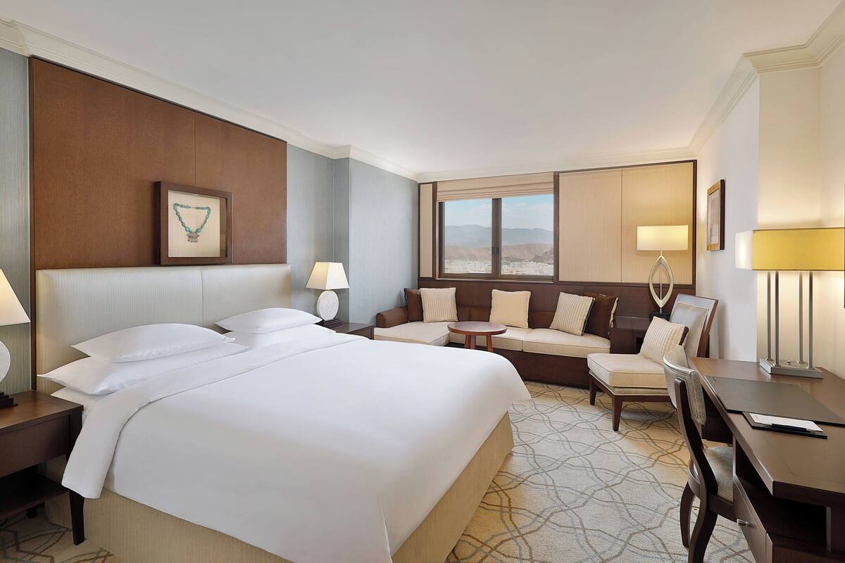 Habitación de hotel con una cama grande, un sofá, un escritorio y vistas a las montañas.