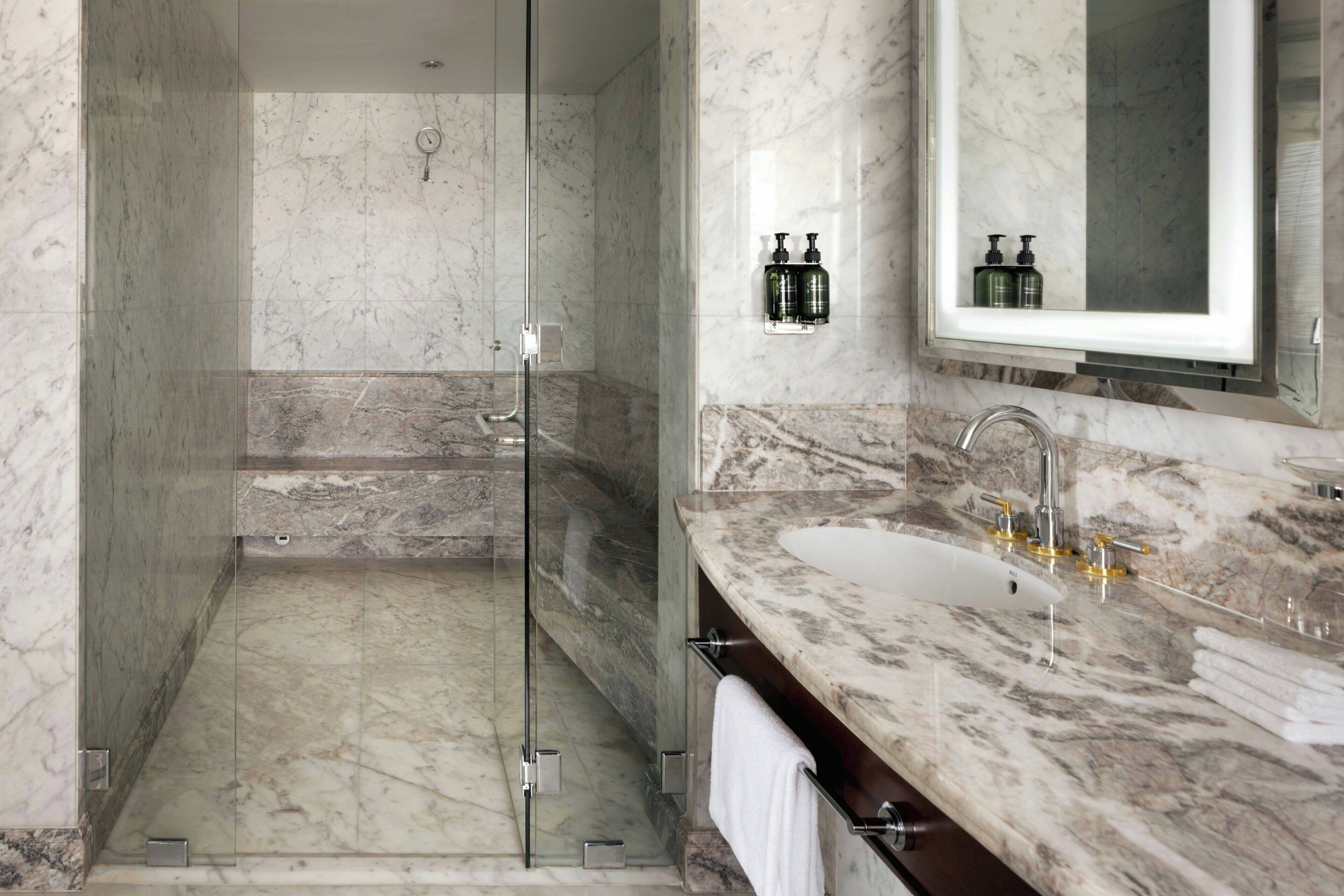 Un baño moderno con ducha envuelta en cristal, encimeras de mármol y un espejo grande.