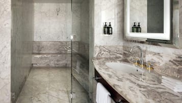 Un baño moderno con ducha envuelta en cristal, encimeras de mármol y un espejo grande.