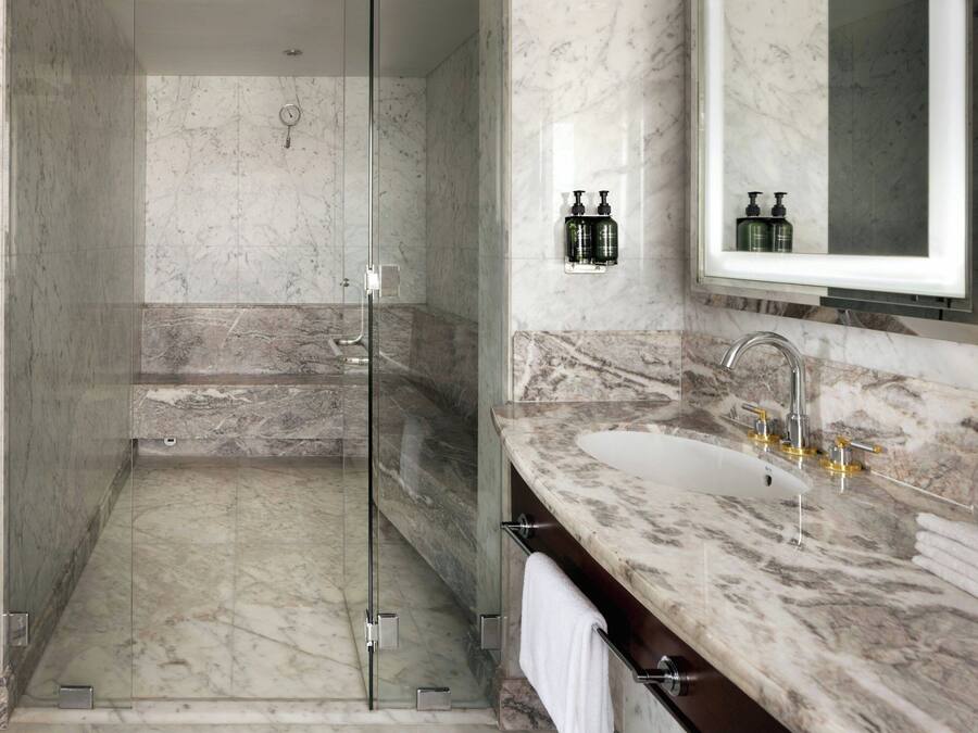 Un baño moderno con ducha envuelta en cristal, encimeras de mármol y un espejo grande.