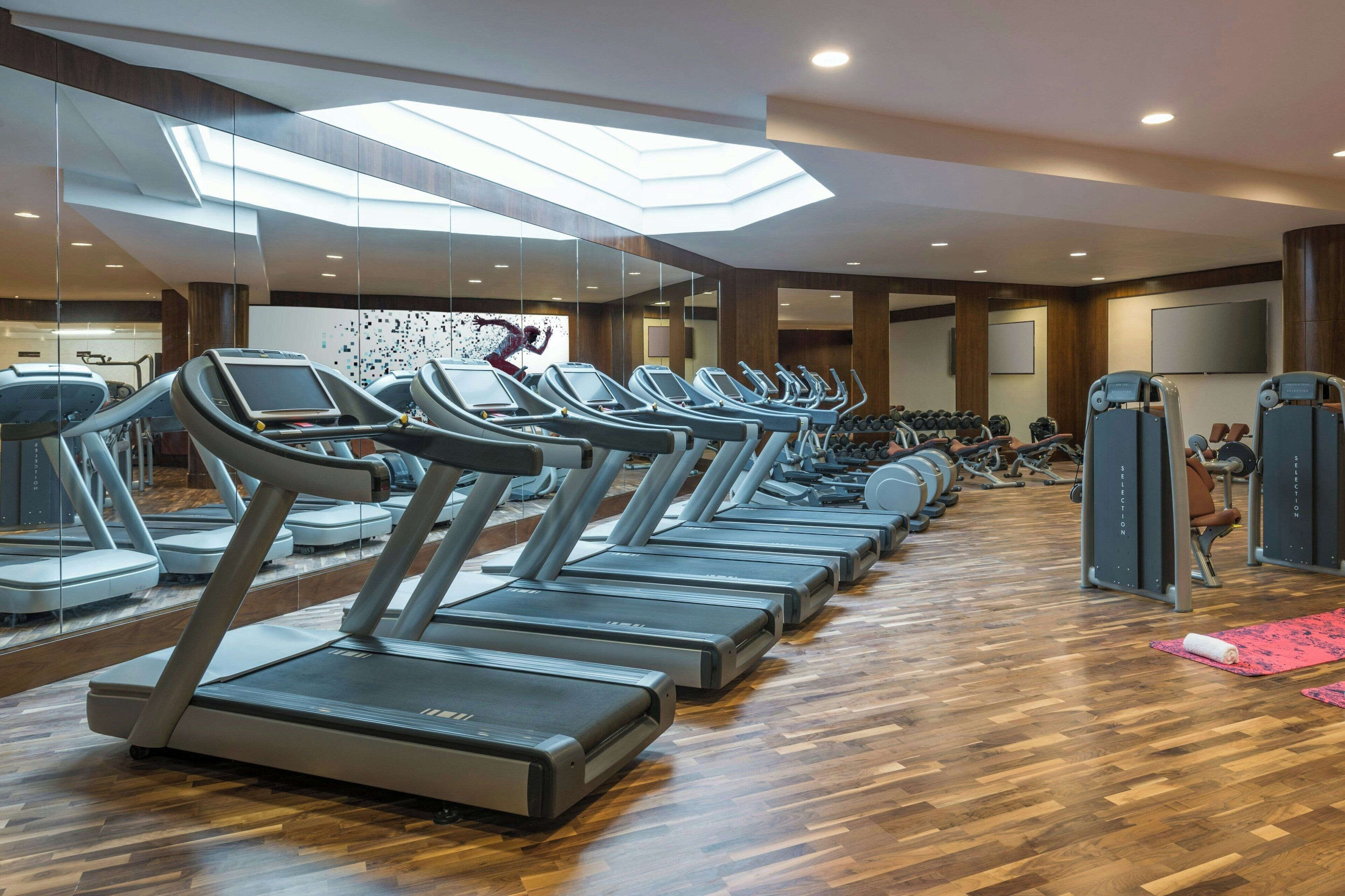 A gym with multiple treadmills, weight machines, and a large mirror wall.