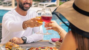 Una taula de menjador amb menjar i begudes, una piscina de fons i ombrel·les exteriors.