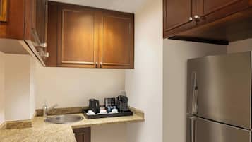 Una cocina con armarios de madera, un refrigerador de acero inoxidable, una cafetera y un lavamanos.