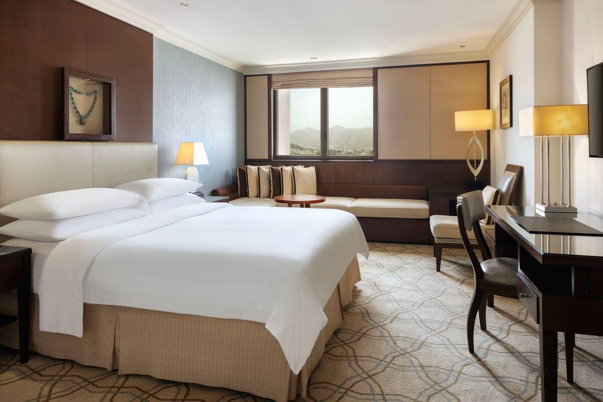 Habitación de hotel con una cama grande, un escritorio, una silla, una mesita, un sofá y una ventana con vistas.