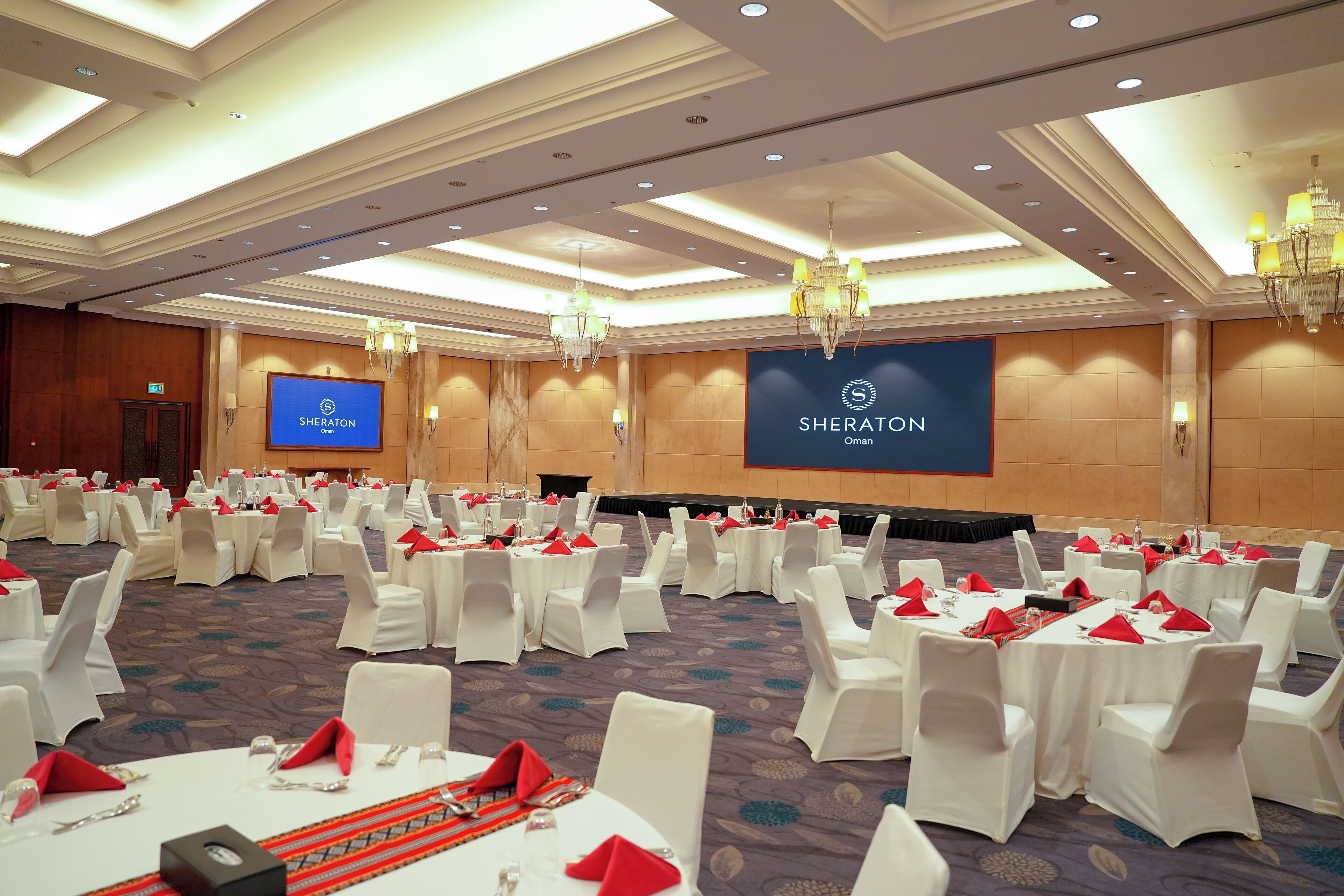 Un salón de conferencias con mesas redondas, sillas blancas y servilletas rojas.