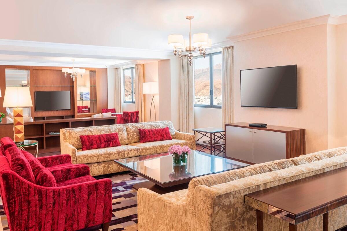 Habitación de hotel con televisor de pantalla plana grande, un sofá, una mesa de centro y un comedor.