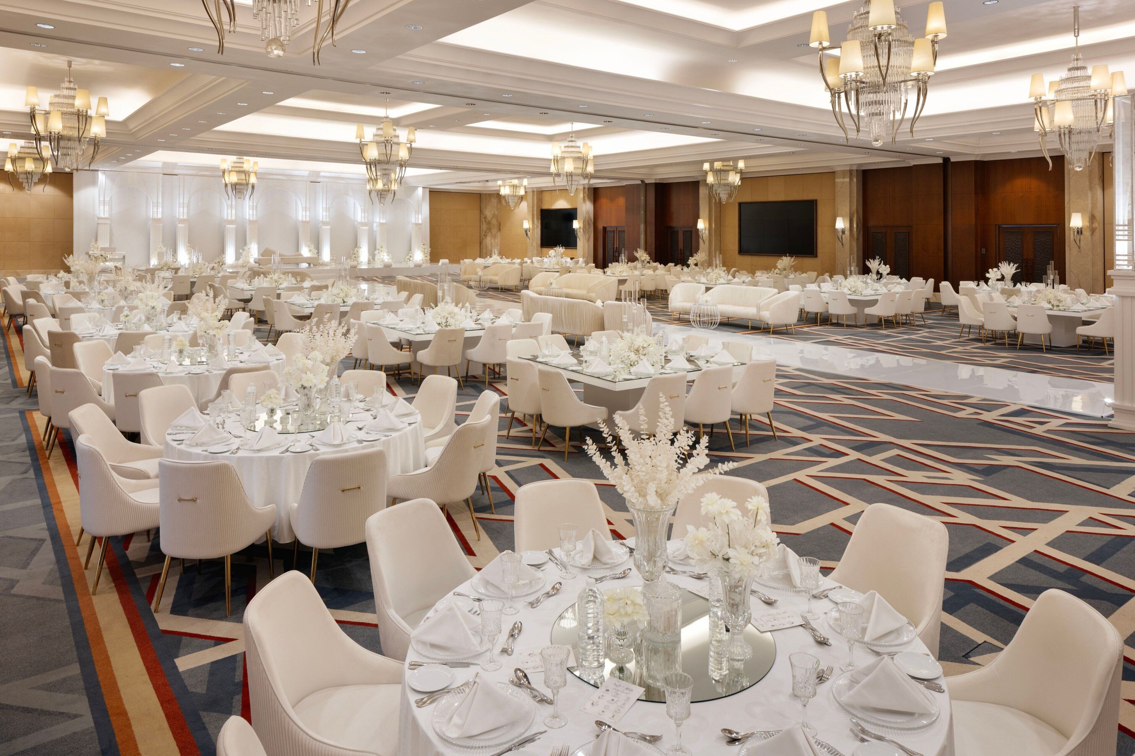 Un salón de banquetes con mesas redondas dispuestas para comer, sillas blancas y candelabros.