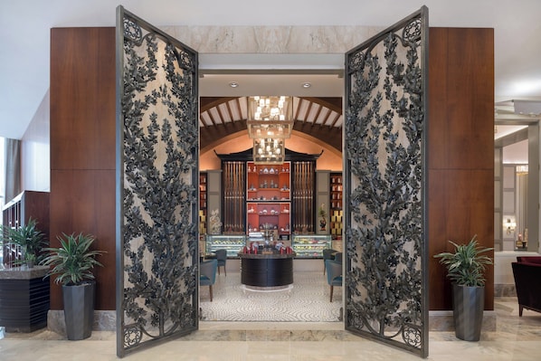 A lobby with a central reception desk, decorative metal panels, and a chandelier.