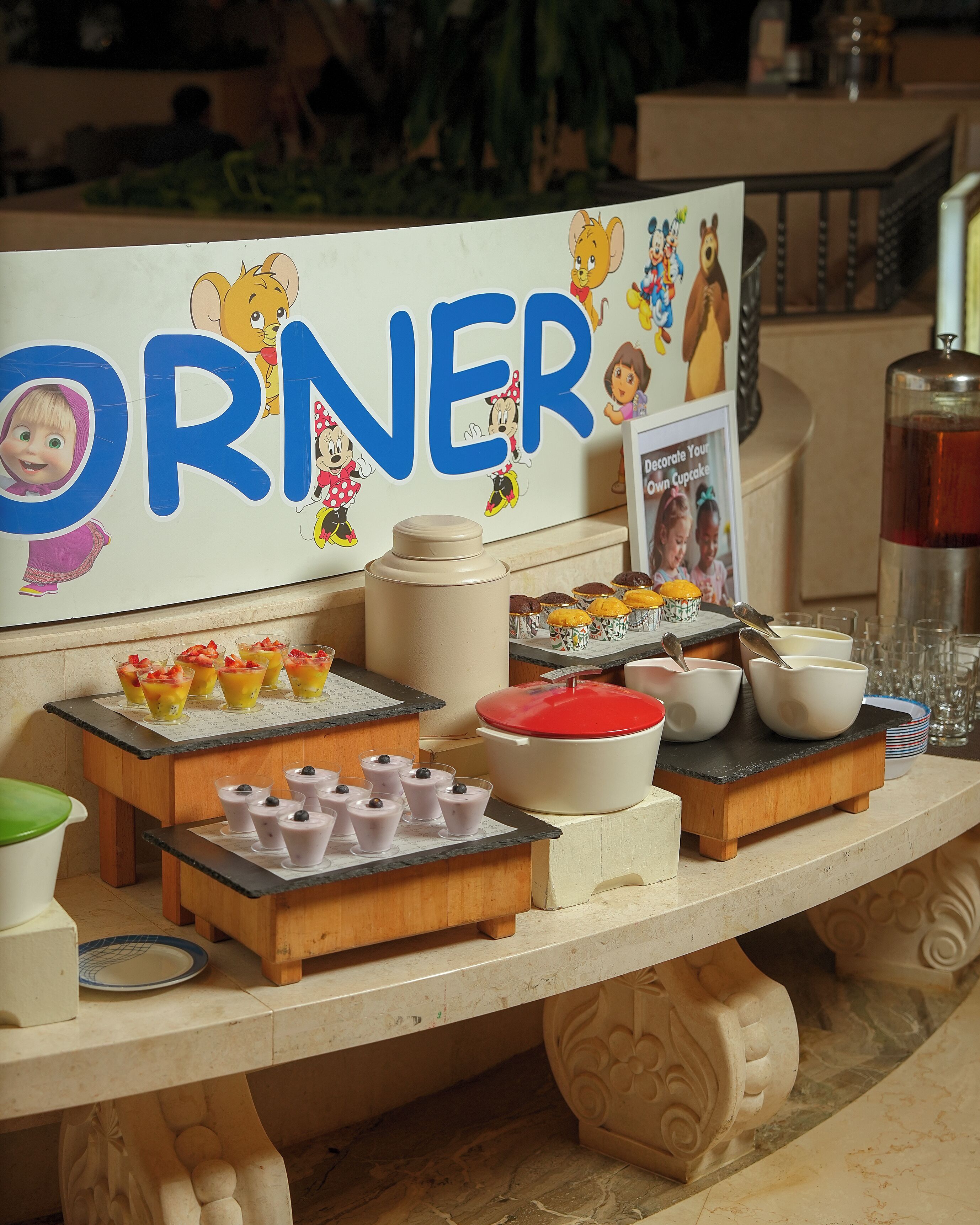 A dessert table with cupcakes, fruit cups, and a sign with cartoon characters.