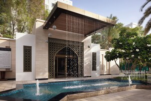 A modern building with a pool, water features, and a white picket fence.