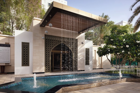 A modern building with a pool, water features, and a white picket fence.