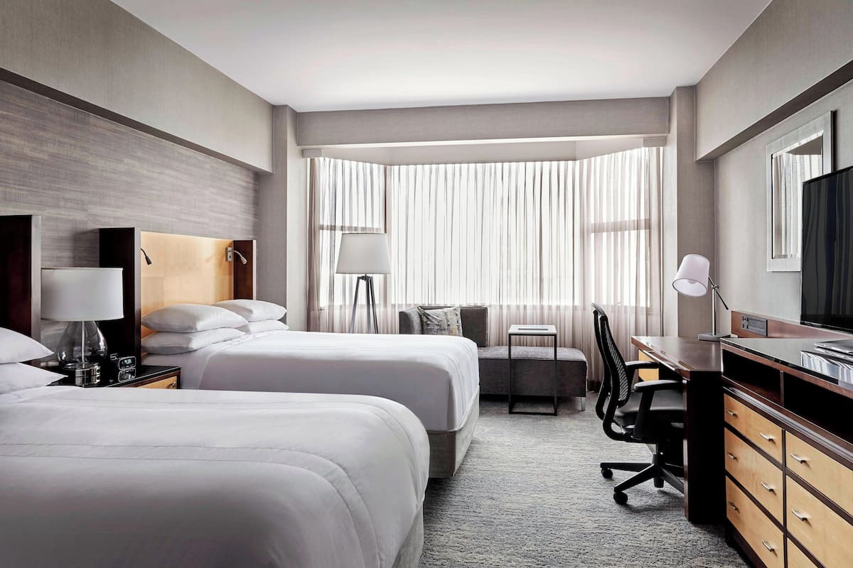 A hotel room with two beds, a desk, a chair, a dresser, and a television.