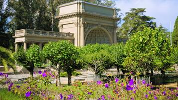 A classical building with columns and a dome, surrounded by lush greenery and purple flowers.