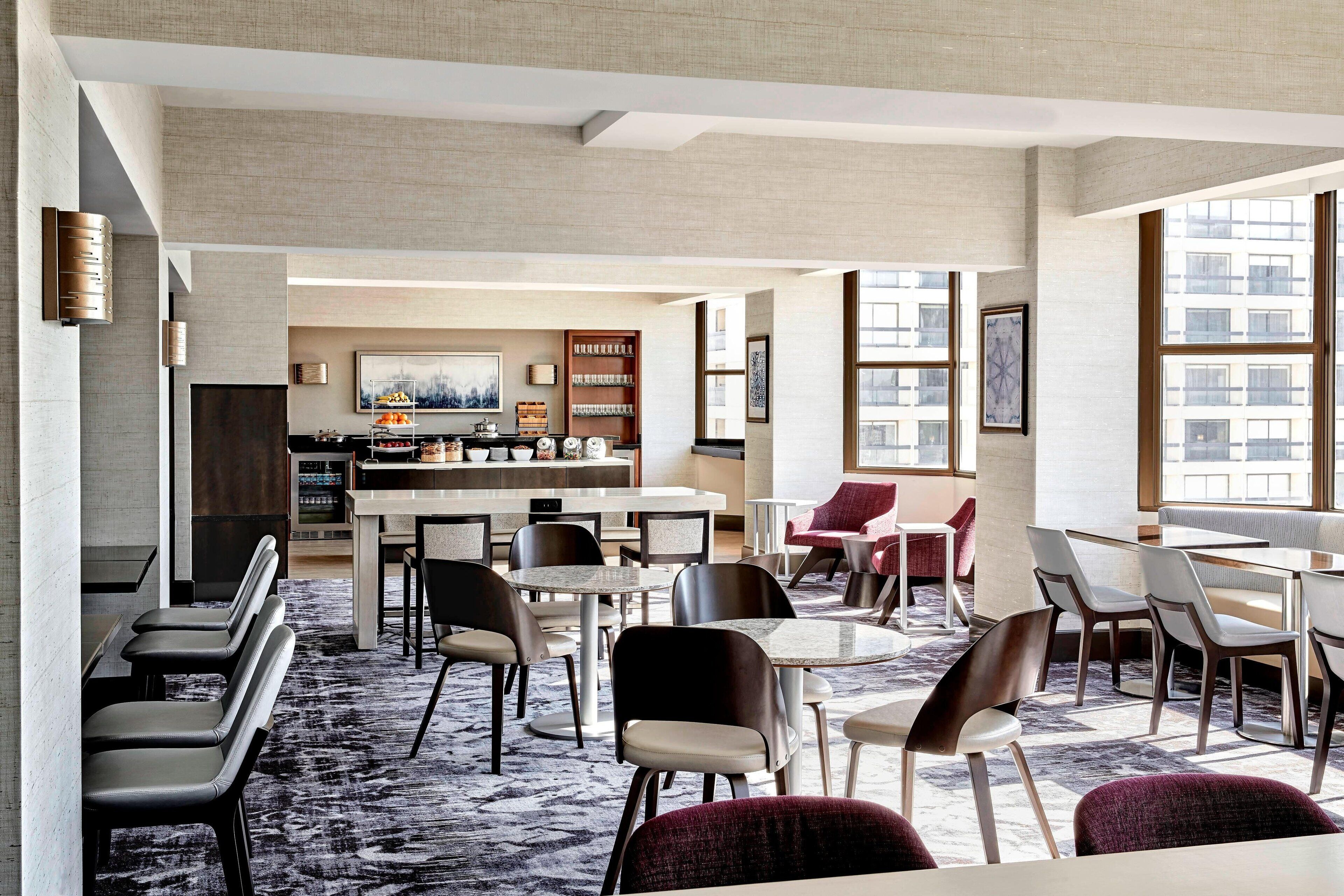A modern hotel lobby with a bar area, seating arrangements, and large windows offering views of the cityscape.