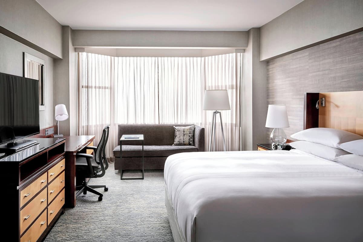 A hotel room with a large bed, a desk with a computer, a sofa, and a TV.