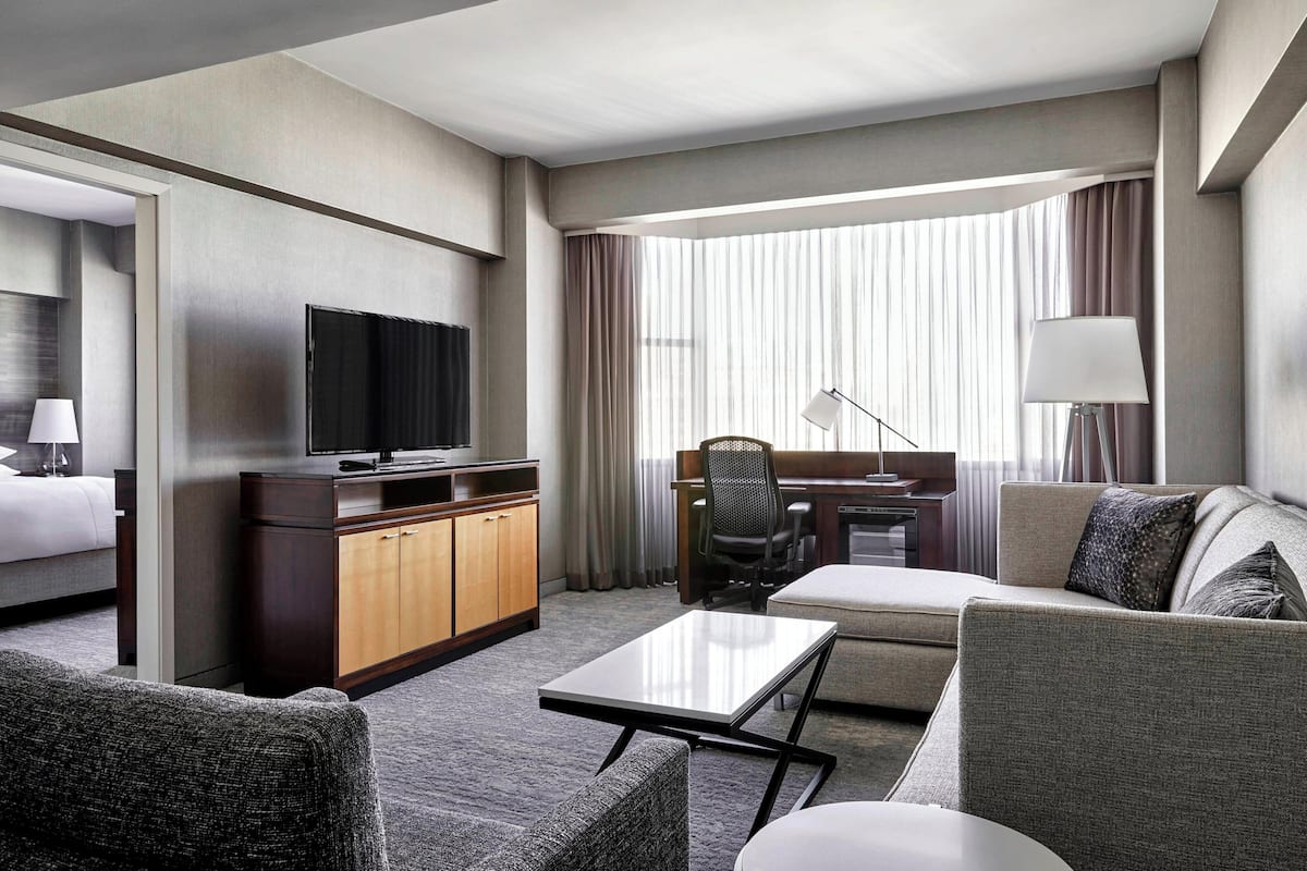 A hotel room with a bed, a desk with a chair, a television, a sofa, and a lamp.
