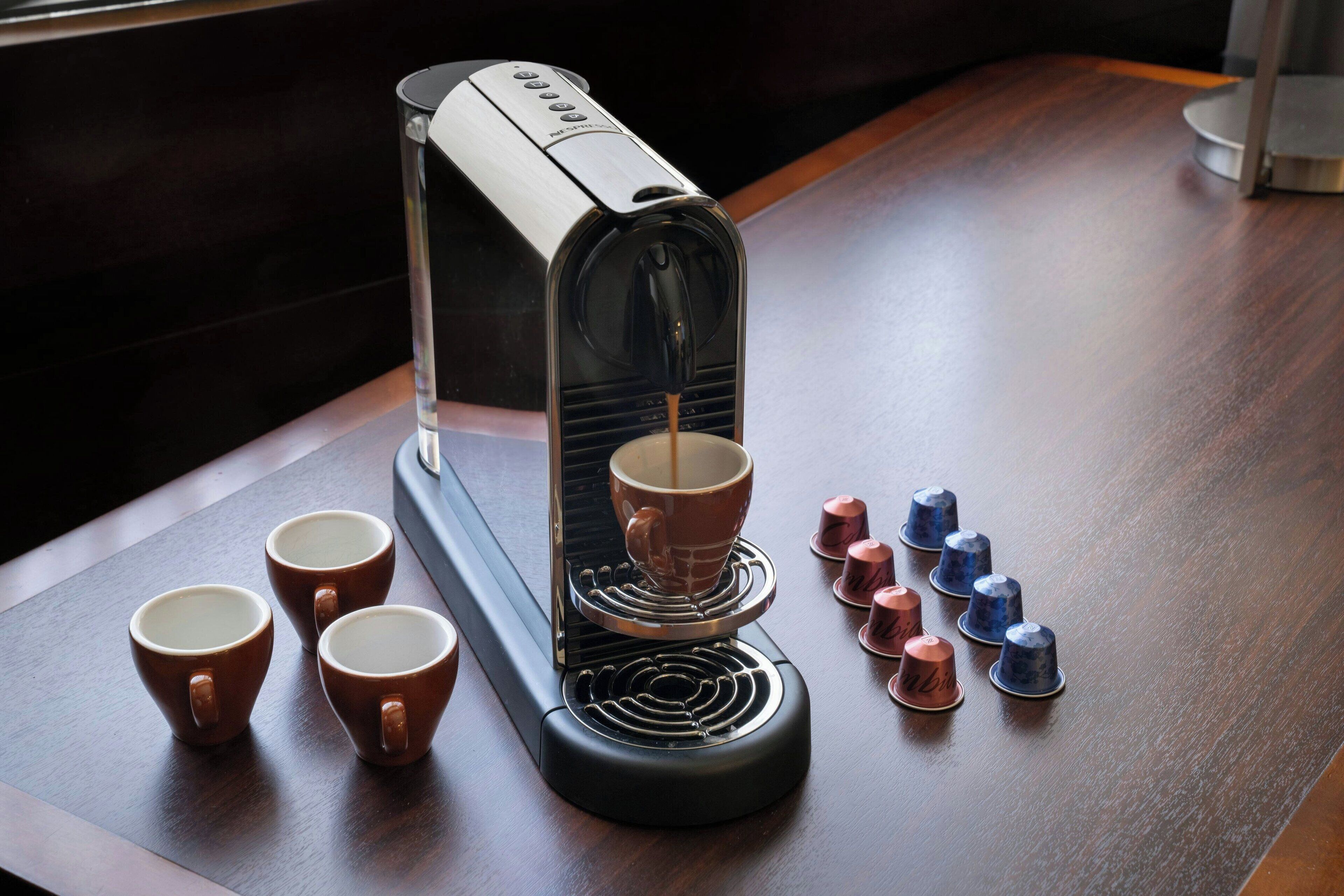 A coffee machine with four cups and six capsules on a wooden table.