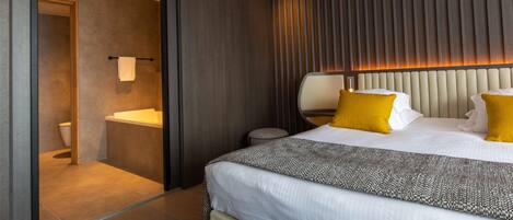 A modern hotel room with a large bed, a bedside table, a mirror, and a view into the bathroom.