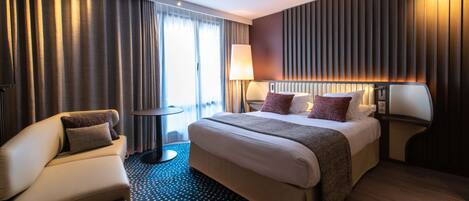 A modern hotel room with a large bed, a sofa, a small round table, and a lamp.