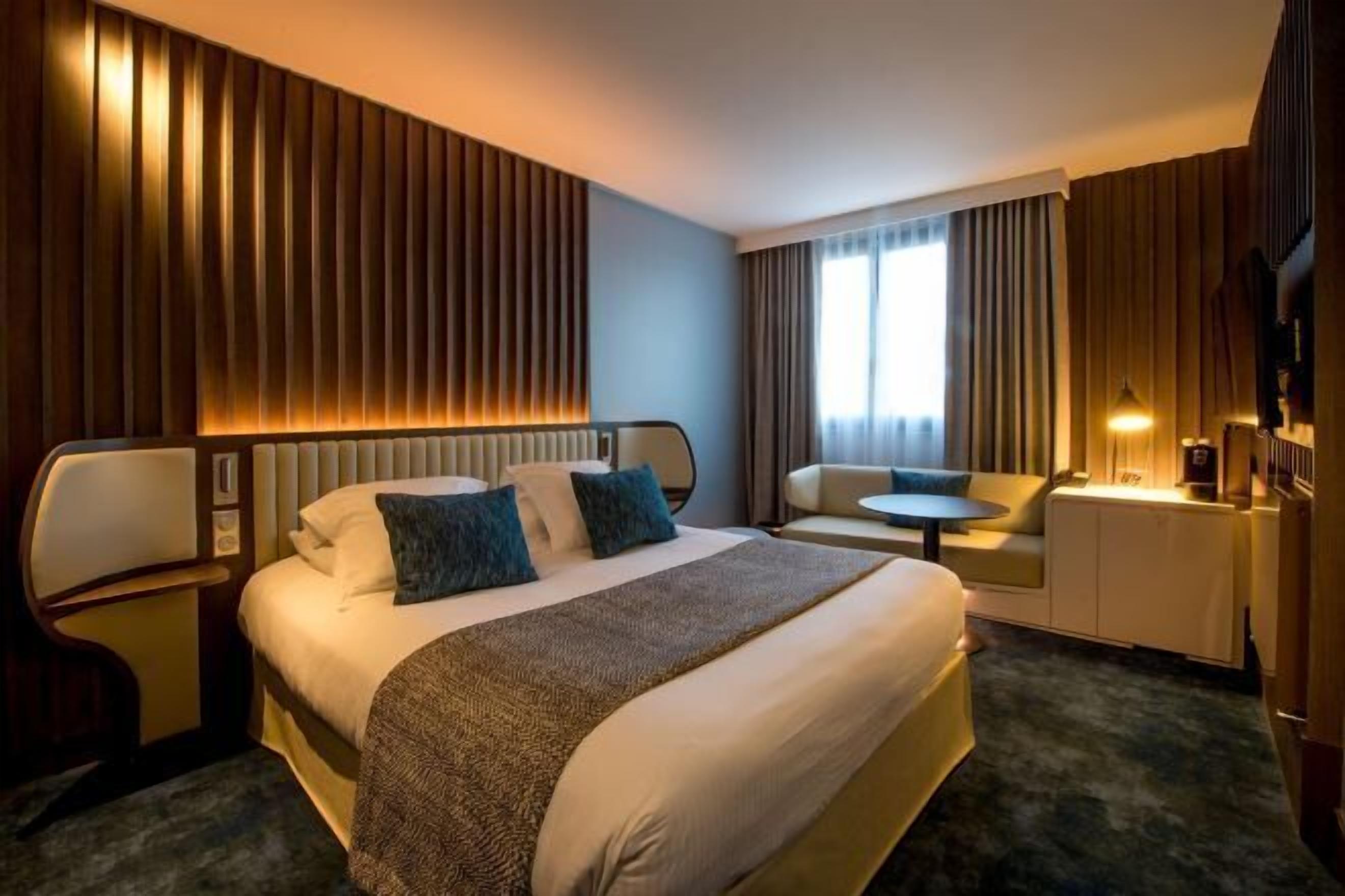 A hotel room with a large bed, a desk, a chair, and a small table.
