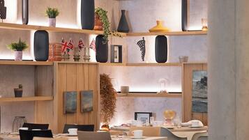 Un comedor moderno con mesas y sillas, estanterías de madera con adornos y un gran pilar.