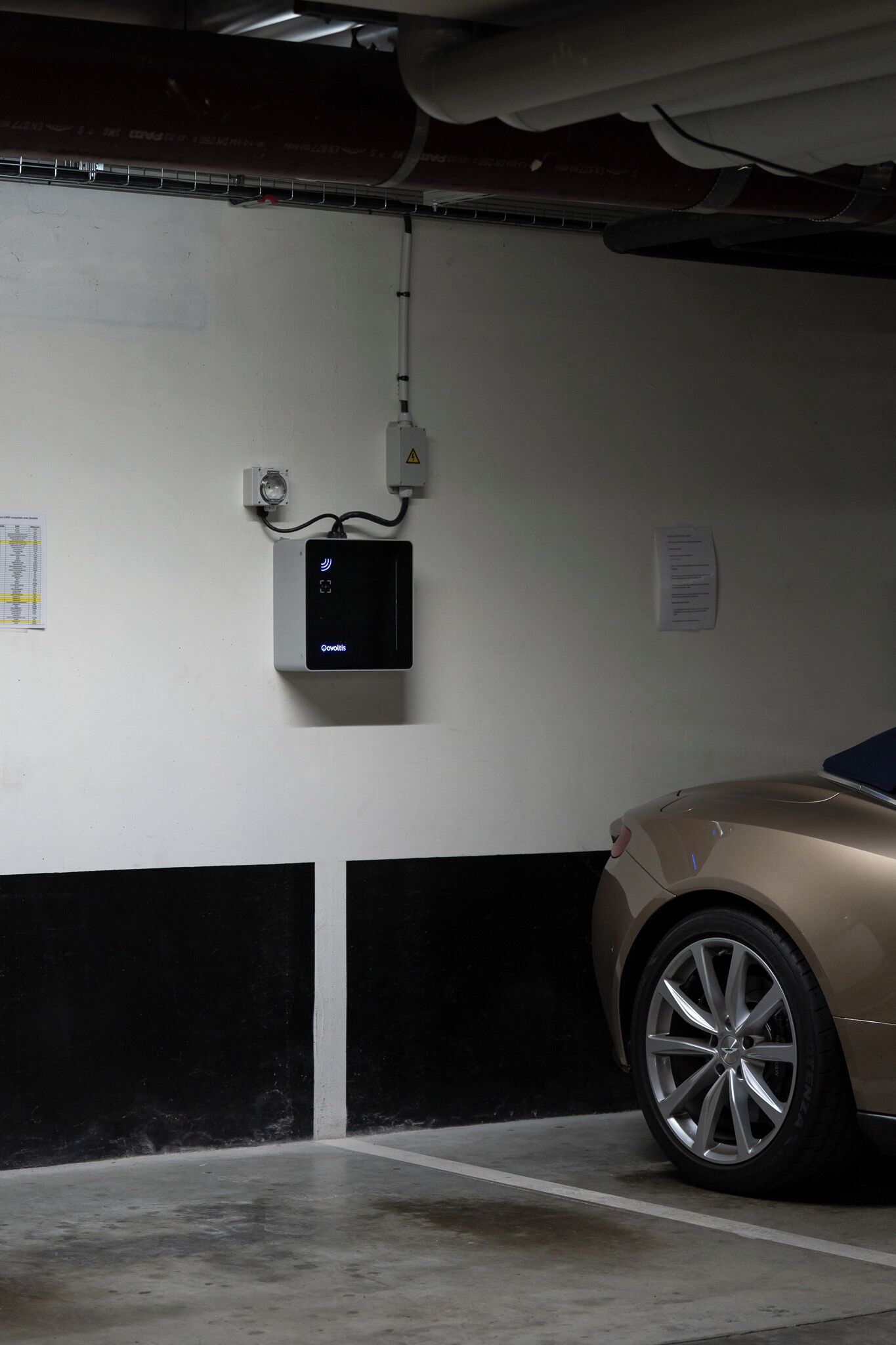Un garaje para coches con un automóvil, una cámara de seguridad y un panel de control en la pared.