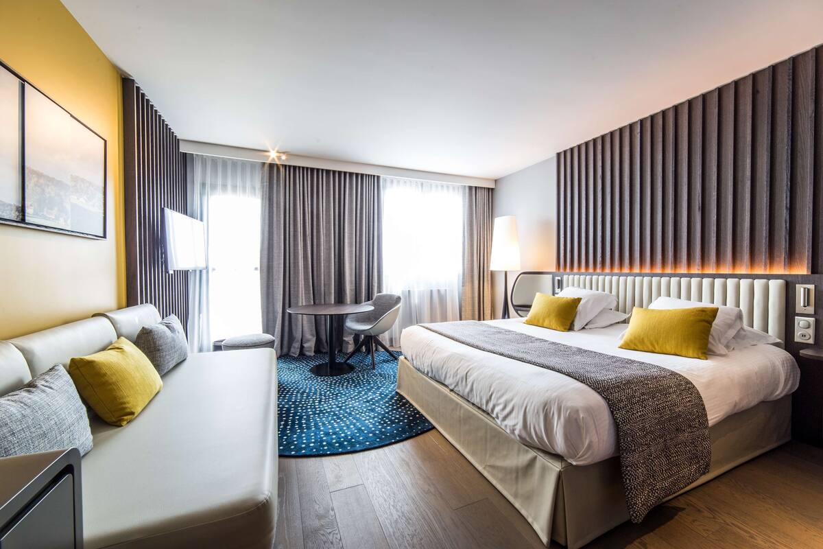 Moderni hotellihuone, jossa on sänky, sohva, pieni pöytä ja tuoli.