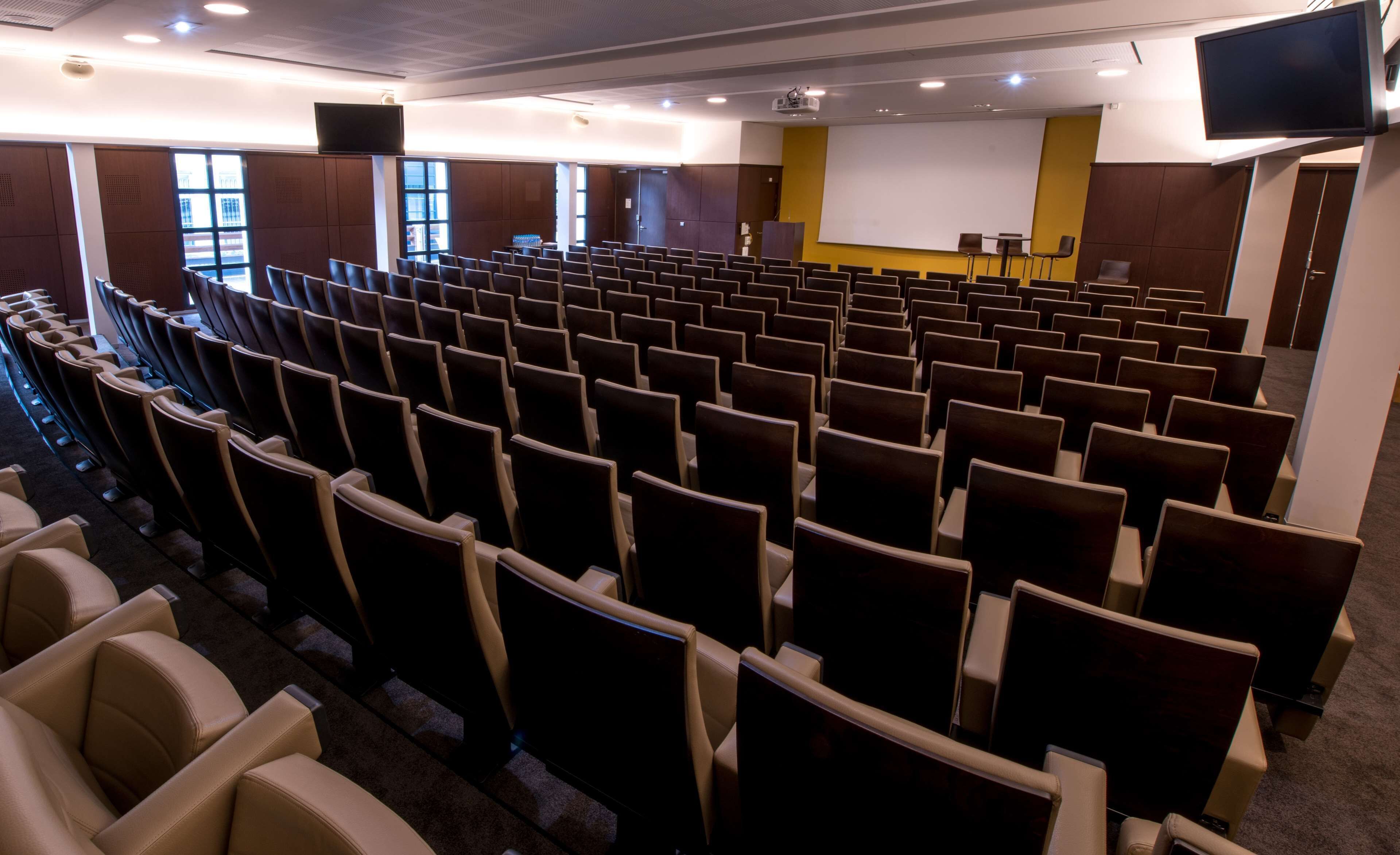 En teater med rader av sittplatser, en scen med en skärm och ett projektionssystem.