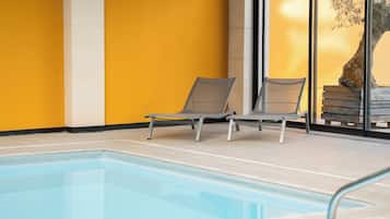 An indoor swimming pool with two lounge chairs and a large window.