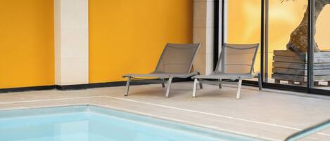 An indoor swimming pool with two lounge chairs and a large window.