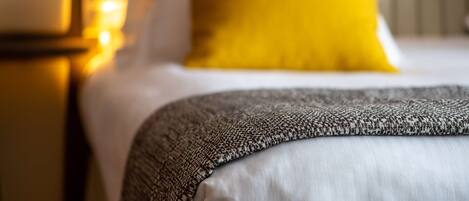 A bed with a patterned throw blanket and a bright yellow pillow.