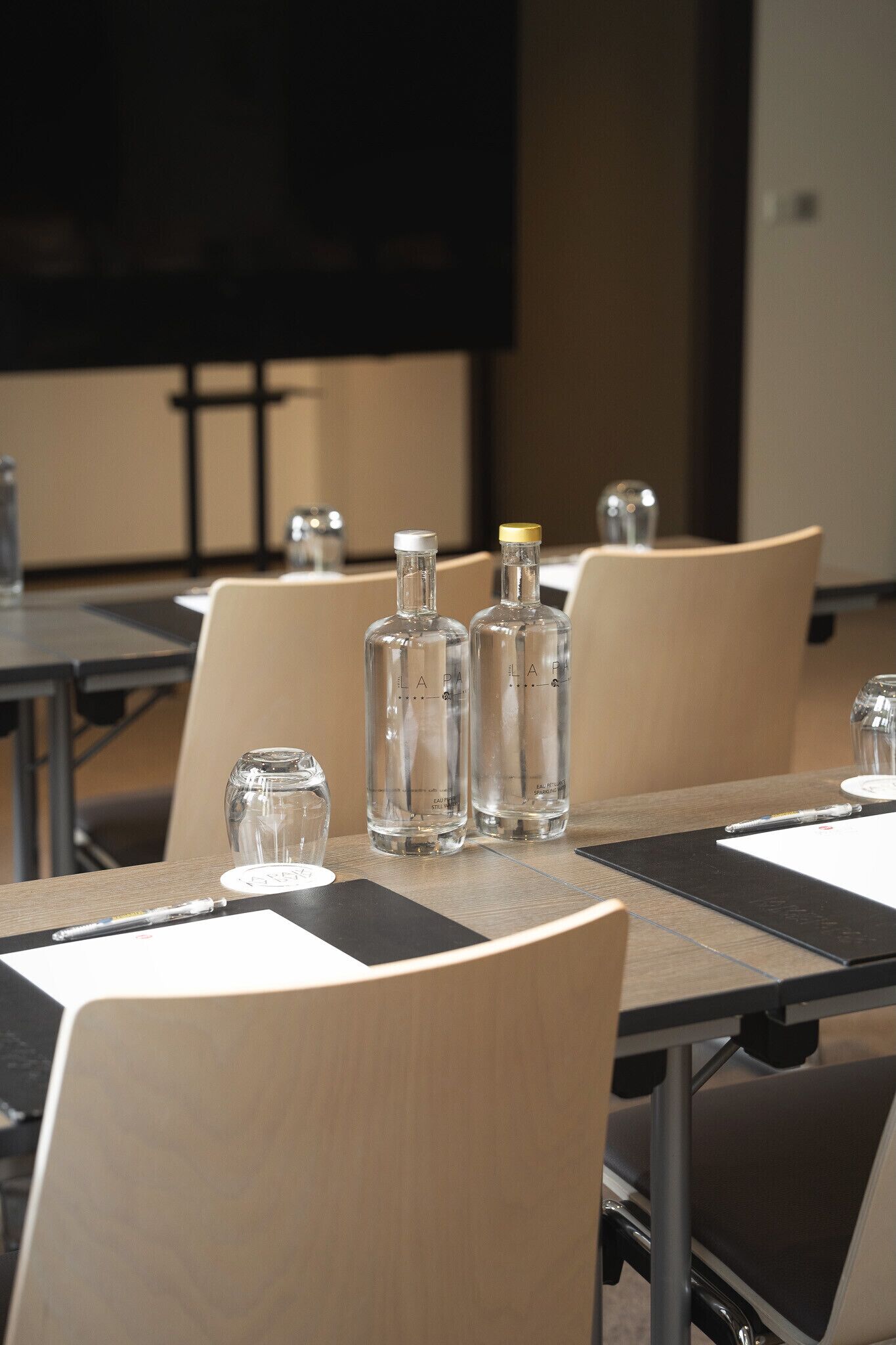 Una sala de conferencias con mesas, sillas y botellas de vidrio transparente sobre la mesa.