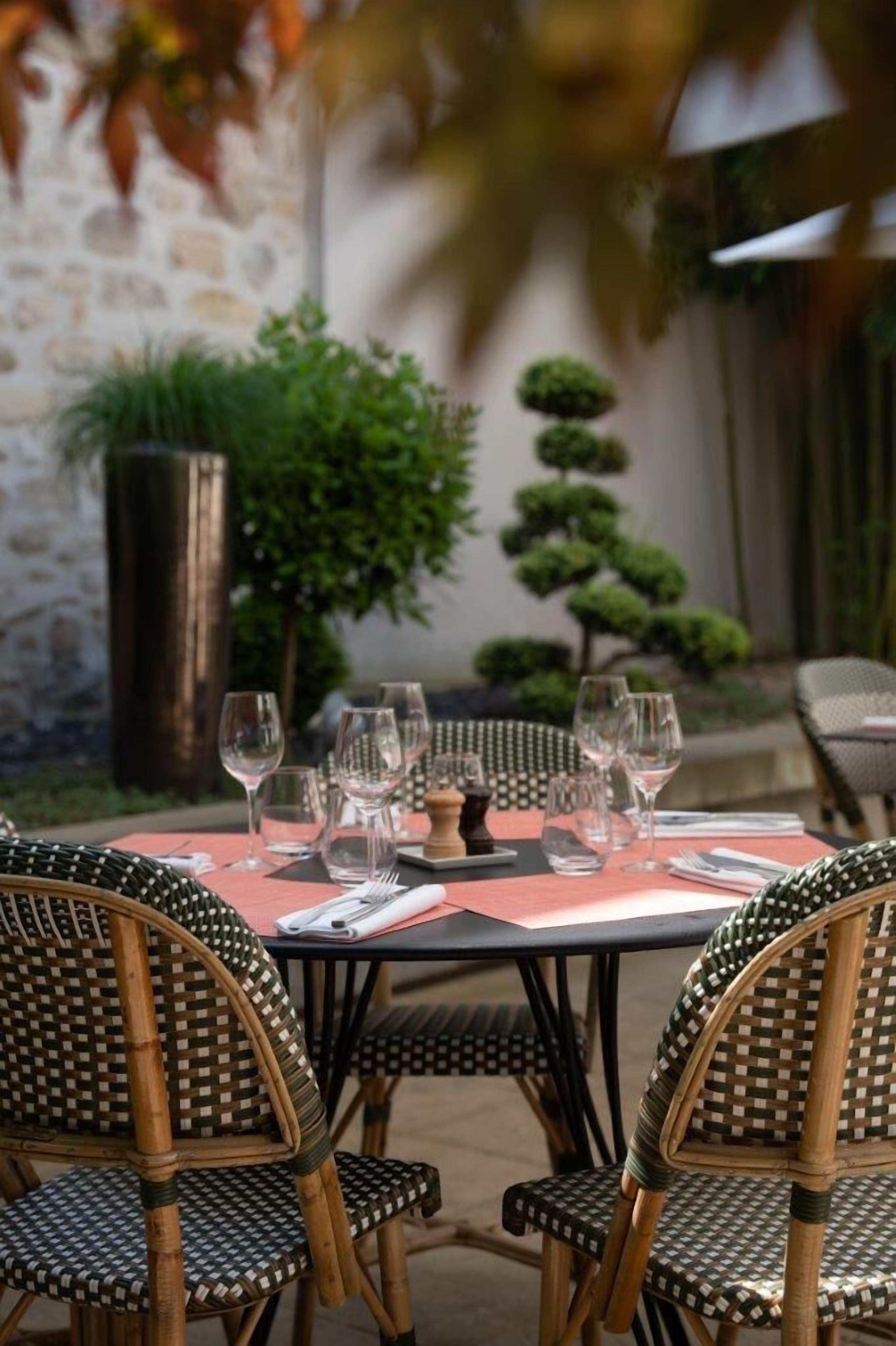 Une table à manger avec des chaises, un mur en pierre et un petit arbre en arrière-plan.